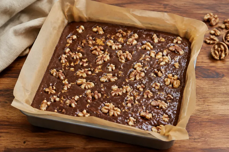 Browniebeslag in de vierkante bakvorm met walnoten over de bovenkant verdeeld
