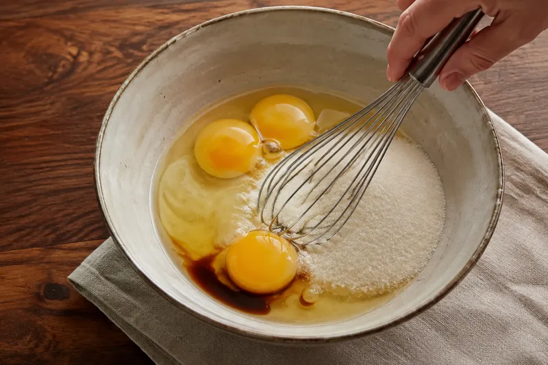 Twee eieren en een extra eidooier worden met fijne suiker gemengd